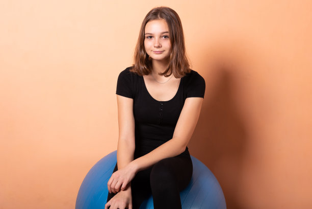 女孩坐在健身球上，背景是浅橙色。图片下载