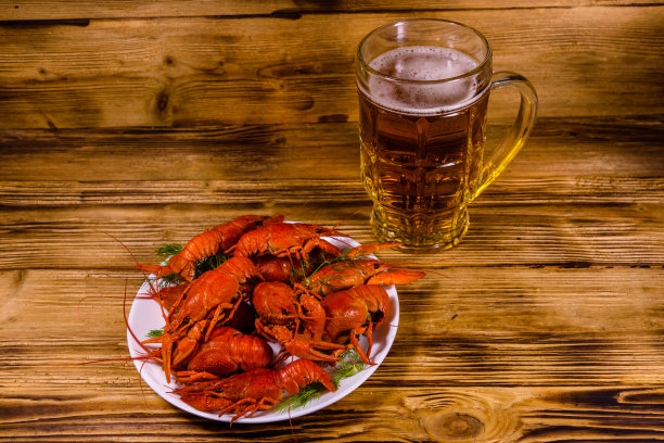 木桌上放着一杯啤酒和煮小龙虾图片下载
