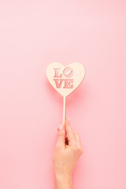 女人手里拿着一颗用天然材料制成的爱心，以粉色的文字为背景。垂直帧复制空间。图片下载
