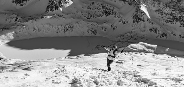一个快乐的女人(游客)的黑白照片与一个背包和冰斧在雪坡上在冬天的山区。冬天的山旅游。图片下载