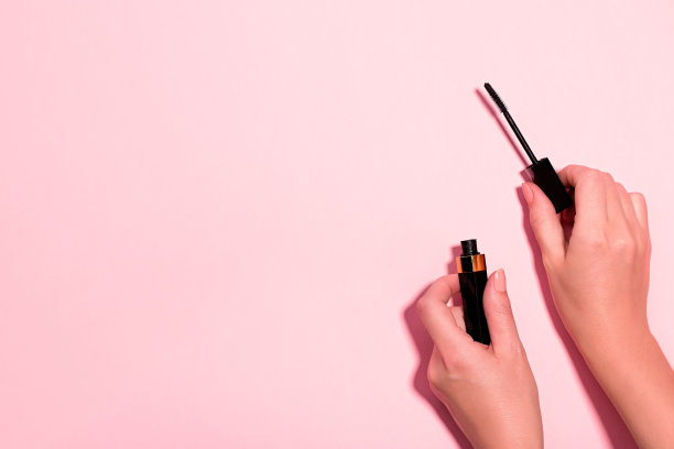 女人的手拿着打开的黑色睫毛膏粉彩背景，俯视图。简约美妆产品背景，平铺，复制空间。眼妆概念图片下载