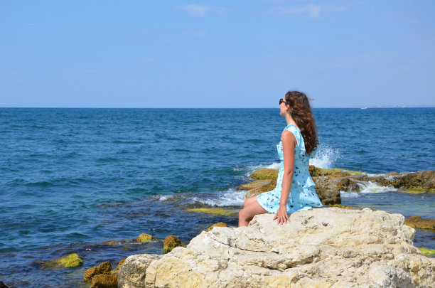 穿着裙子的年轻女子站在布满岩石的海边图片下载