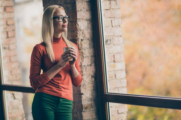 平和的女人工人的侧面照片休息放松拿杯热拿铁看窗户梦想周末穿红色高领毛衣在公司办公室阁楼图片下载