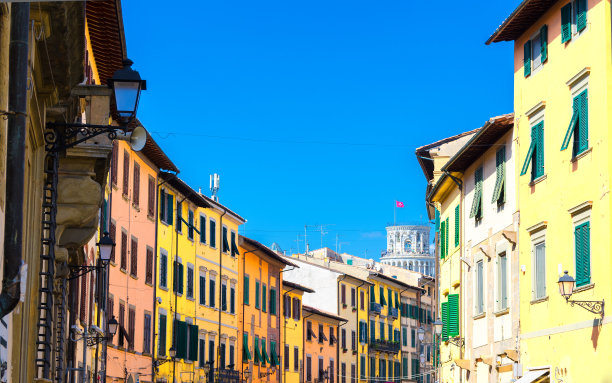 意大利托斯卡纳，阳光明媚的日子里，比萨城历史中心街道上一排排五颜六色的建筑，背景是斜塔和湛蓝的天空图片下载