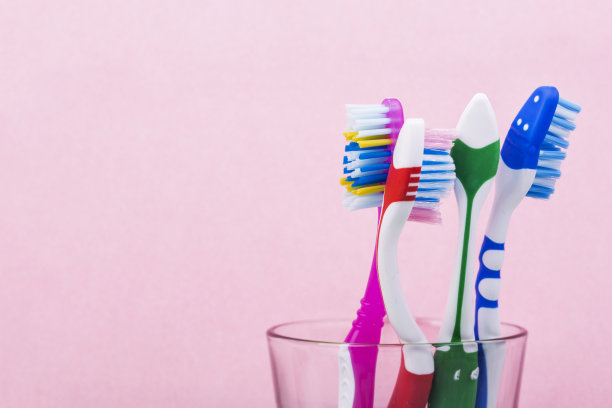 近距离拍摄的一套彩色牙刷在一个玻璃上粉红色的背景，概念牙科图片下载