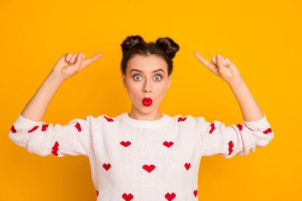 特写照片的美丽的女士表明手指在新的沙龙发型不喜欢两个发髻准备浪漫的约会穿心形图案白色红色毛衣孤立的黄色背景图片下载