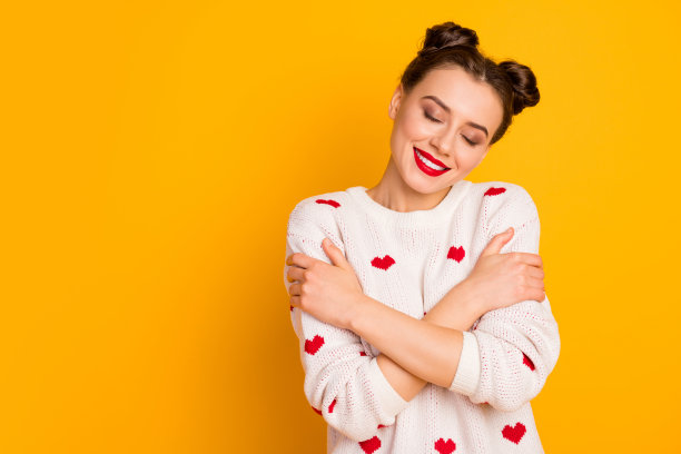美丽的女士的照片拥抱自己的肩膀，眼睛闭上，享受触摸套头衫，柔软的穿心形图案，白色，红色针织毛衣孤立的黄色背景图片下载