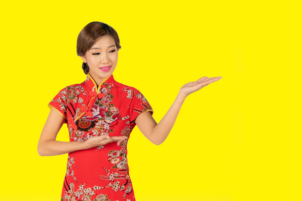 漂亮的亚洲女性与中国传统服装旗袍或旗袍手显示空白。春节观念，女模特孤立在黄色背景上。图片下载