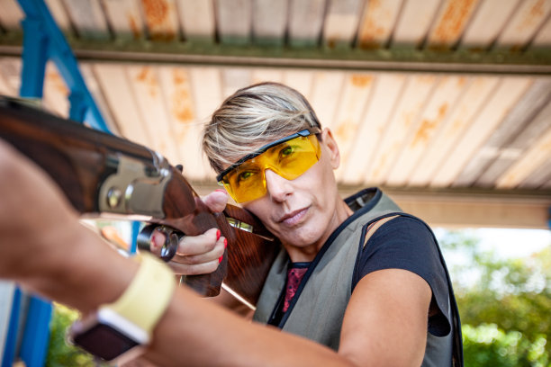 肖像成年妇女双向飞碟射击指导员瞄准与猎枪在运动训练班-库存照片图片下载