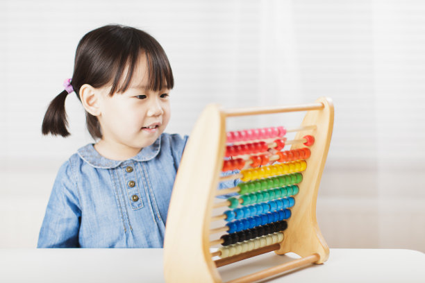 蹒跚学步的小女孩在白色背景下玩算盘学习数学图片下载