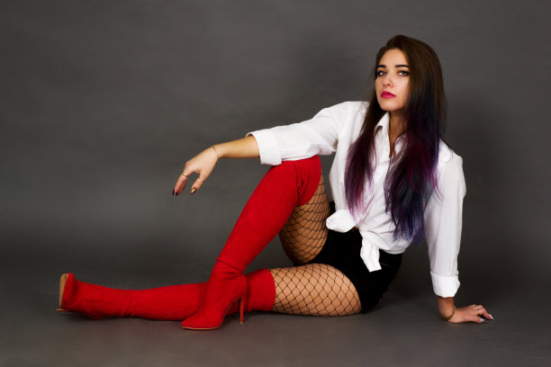 深褐色的女孩穿着白色的衬衫和红色的靴子和长筒袜在一个大网眼在一个灰色的工作室背景全高。图片下载