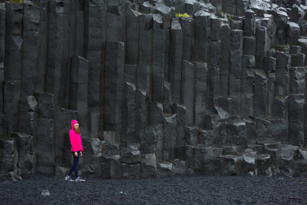 一名亚洲妇女站在冰岛黑海滩玄武岩柱上的照片。Reynisfjara海滩，冰岛最美的黑色沙滩图片下载