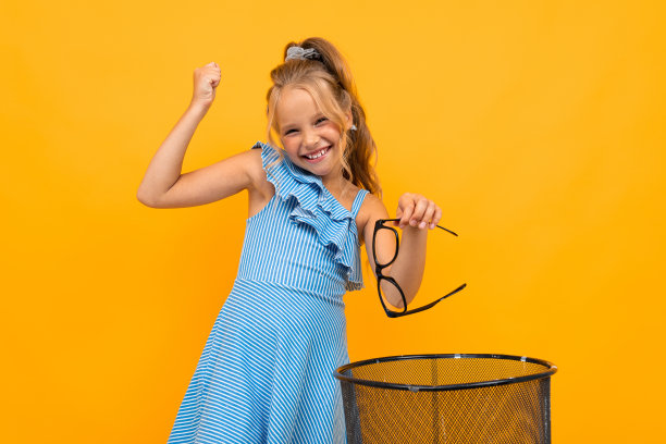 迷人的金发女孩把眼镜扔进黄色墙上的垃圾桶里图片下载
