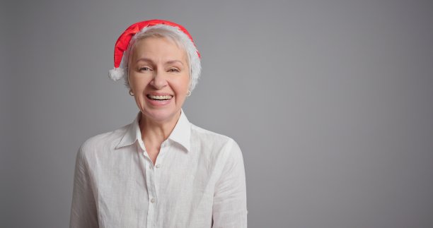 戴着圣诞老人帽的迷人老妇人在灰色背景下大笑图片下载