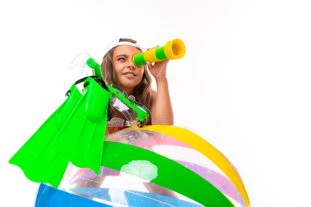 女孩拿着潜水员的脚蹼，通过双筒望远镜看，并靠在一个充气条纹球上游泳在一个白色的背景图片下载