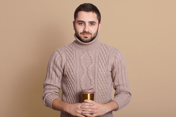 年长的白人男子拿着咖啡杯的摄影棚照片，米色背景，英俊的男子手持保温杯，享受热饮，看着镜头，看起来很自信。图片下载