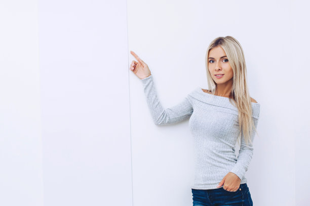 漂亮的金发美女穿着毛衣和牛仔裤在白色的背景点手指图片下载