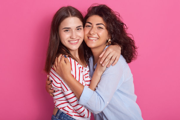 水平的照片，漂亮的年轻朋友与深色头发，看着微笑直接对着相机。波浪形头发的女士穿蓝色衬衫，直发的女孩穿红色条纹休闲衬衫。图片下载