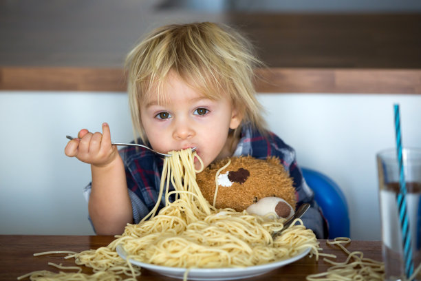 小男孩，蹒跚学步的孩子，午餐吃意大利面，喂泰迪熊朋友图片下载