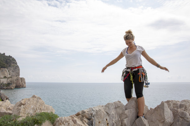 一名年轻的攀岩者在海面上攀爬的顶端高兴地伸展四肢图片下载