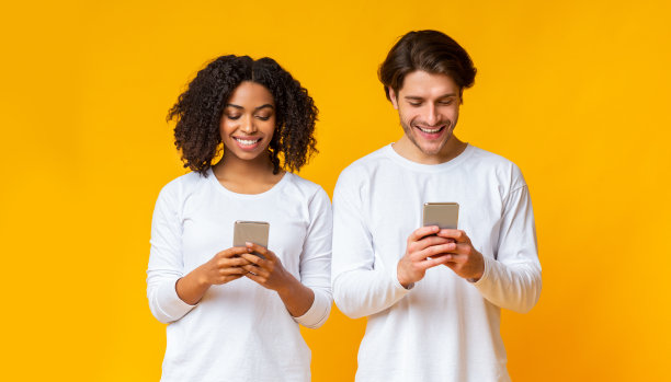 微笑的异族情侣忙着他们的智能手机，沉迷于电子产品图片下载