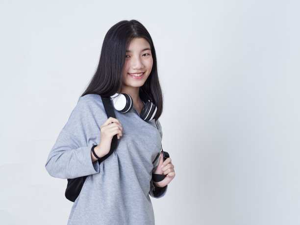 可爱的时髦女孩戴着耳机听音乐，背包孤立的白色背景。图片下载