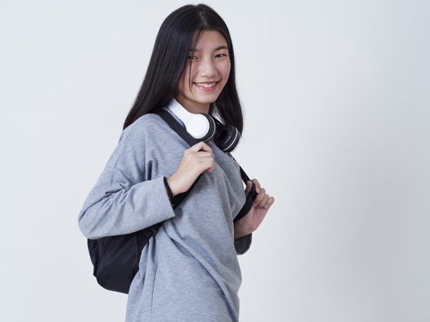 可爱的时髦女孩戴着耳机听音乐，背包孤立的白色背景。图片下载