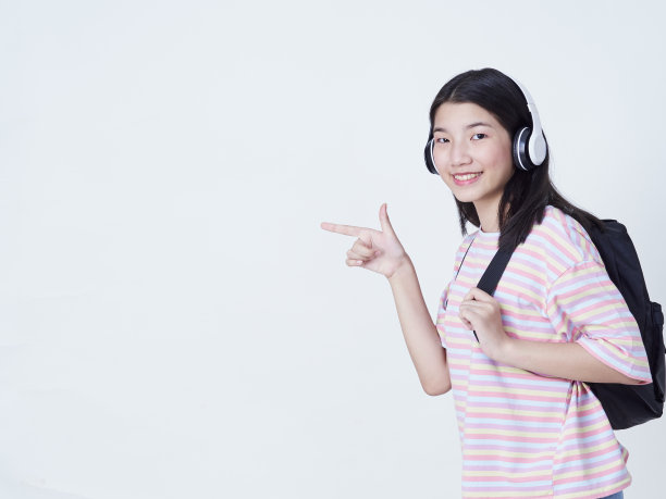 可爱的时髦女孩戴着耳机听音乐，背包孤立的白色背景。图片下载