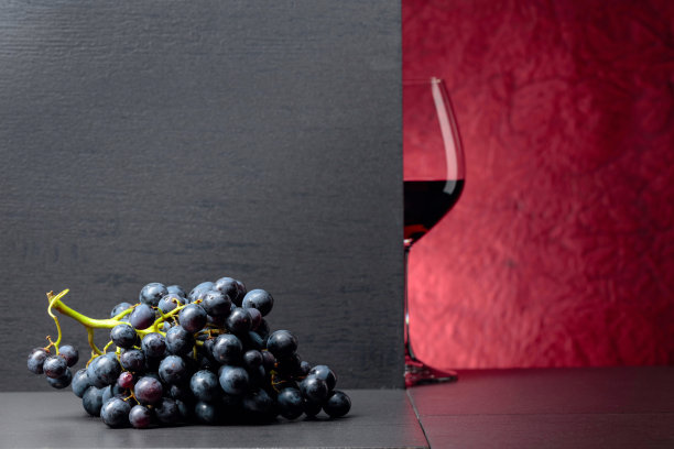 黑色的桌子上放着蓝色的葡萄和一杯红酒。图片下载