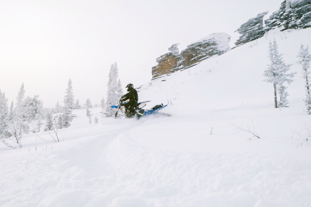 在积雪覆盖的山坡上骑雪地车的人。晴雾，冬季白天户外活动图片下载