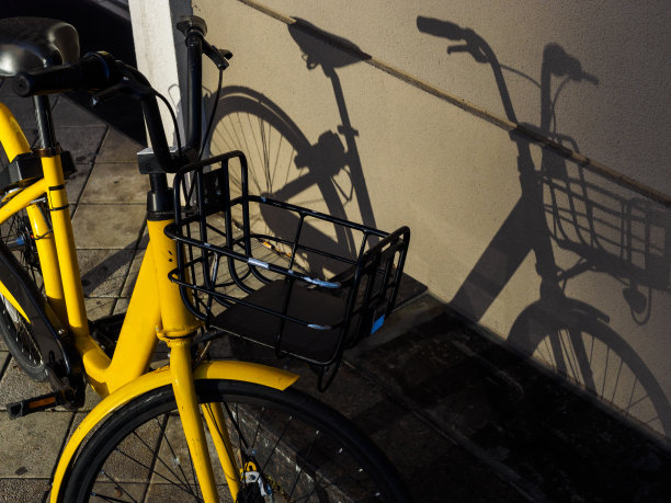 一辆带篮子的黄色自行车靠墙站着，投下了影子图片下载