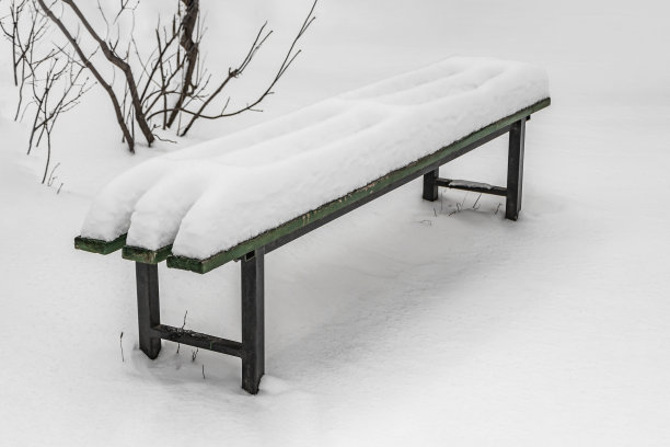 冬天的公园里，一条被漆成绿色的长凳，上面有黑色的铁腿和白色的雪图片下载