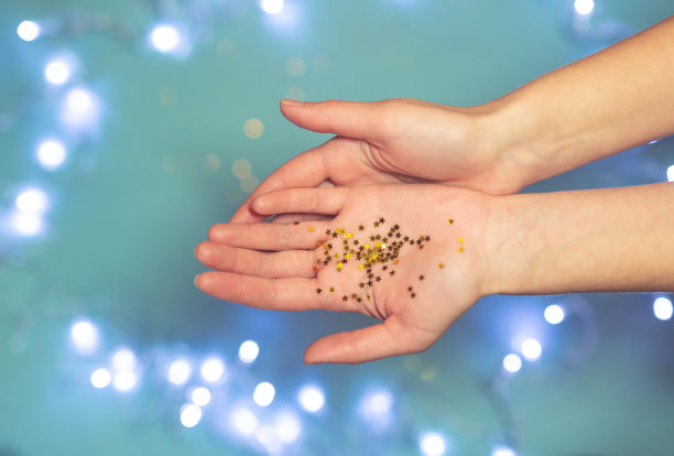 在蓝色背景下，摊开的手掌上有闪闪发光的小金色星星。图片下载