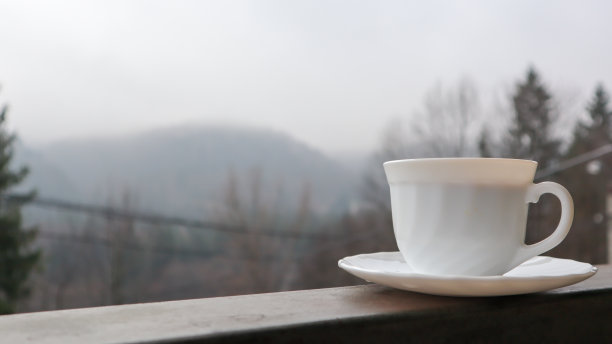 白色的咖啡杯在抽象的自然背景上。阳台上有一个咖啡杯，可以看到后面的自然风光。酒店阳台上的陶瓷杯图片下载