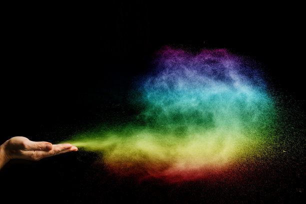 彩色尘埃粒子膨胀与手在黑色背景。图片下载