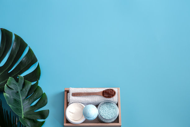 水疗中心。身体护理项目的蓝色背景与热带树叶。夏季配件。空间的文本。图片下载