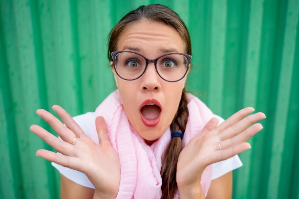 年轻女子在绿色背景下尴尬地看着相机-库存照片图片下载