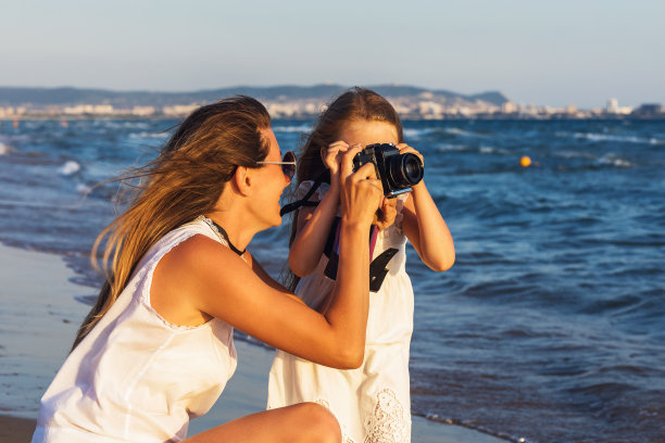 在一个温暖的夏夜，妈妈和女儿在海滩上拍照图片下载