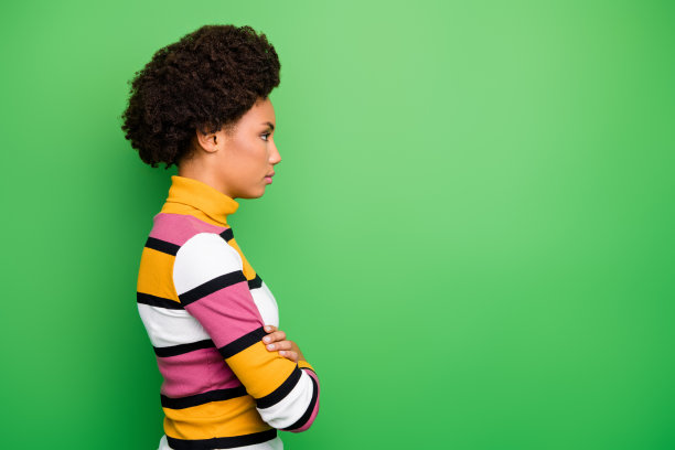 档案照片漂亮的黑皮肤卷曲的商务女士双臂交叉看着严肃的空空间负责的工人穿休闲条纹套头衫孤立的绿色背景图片下载