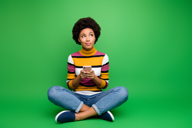 全尺寸照片头脑非裔美国女孩坐着双腿交叉折叠用手机写博客思考类型社交媒体帖子穿牛仔牛仔裤衣服孤立的绿色背景图片下载