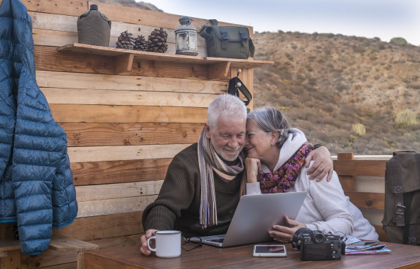 两个人白发苍苍地看着木桌上的笔记本电脑。一对温柔的老夫妇在乡村山间酒吧停下来，然后继续徒步旅行。他们深情地拥抱着对方。图片下载
