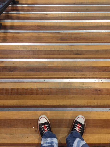 从一个现代的木制楼梯的顶部往下看，台阶上是无法辨认的人的鞋子和定制的牛仔裤图片下载