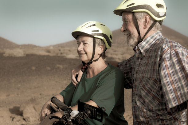 两个戴着黄色头盔微笑的老人骑着自行车享受徒步旅行。干旱的热带景观。活动与健康概念图片下载