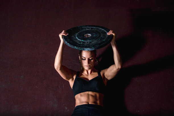 年轻强壮，流汗，适合肌肉发达的女孩与大肌肉做仰卧起坐与杠铃重量板腹部肌肉或腹肌艰苦交叉锻炼训练在健身房地板上从上面看图片下载