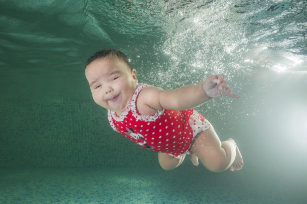 一个穿着红色游泳衣的小女孩在游泳池里学习游泳。婴儿在游泳池里游泳。健康的家庭生活方式和儿童水上运动。儿童发育，疾病预防素材图片