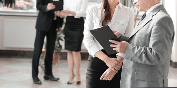 商务人员和助理站在现代化的办公室里讨论工作文件图片下载