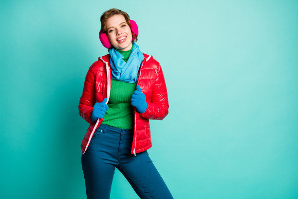 漂亮可爱的照片可爱的女士享受阳光明媚的冬天滑冰度过自由时间的喜悦穿休闲的红色大衣蓝色的围巾粉红色的耳朵覆盖裤子孤立的蓝绿色的背景图片下载