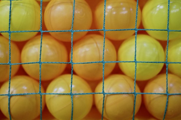 绿色网后面是黄色的塑料球。这些球是大量的黄色塑料球，以背景的形式紧贴在绿色网孔的后面。图片下载