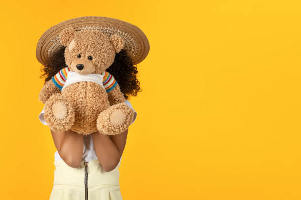 可爱的小女孩躲在泰迪熊玩具孤立的黄色背景图片下载