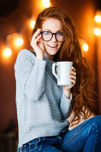 身穿牛仔裤和毛衣的女人坐在椅子上喝咖啡特写图片下载